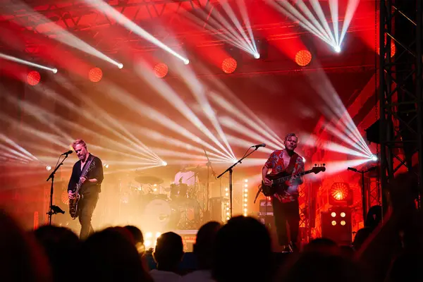 stock image Silhouettes of crowd at concert in front of stage with bright spotlights. People enjoy live music at the bands performance. Concert hall with musicians on stage and fans during music festival