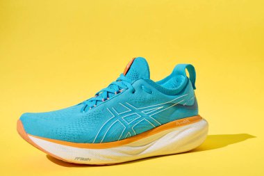 Tek mavi Asics jel-Nimbus 25 spor ayakkabısı. Katı sarı arka planda gölgesi var. Şık ayakkabılar. Modaya uygun minimalizm konsepti. Katy Wroclawskie, Polonya - 12 Mayıs 2024