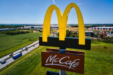 McDonald 's McCafe tabelasının havadan görünüşü işlek otoyolun yanında duruyor. Arka planda açık mavi gökyüzü ve tarım alanları var. McDonald 's restoranı. Katy Wroclawskie, Polonya - 14 Mayıs 2024