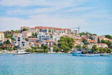 Yamaçta açık mavi sular boyunca yanaşmış tekneleri olan renkli kıyı evleri olan deniz kenarı kasabası. Adriyatik Denizi 'nde yaz tatili için konutlar. Rogoznica, Hırvatistan - 14 Temmuz 2024
