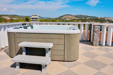 Outdoor hot tub on sunny rooftop deck with bubbling water and comfortable seating with beautiful view on touristic cityscape. Place for relaxation and leisure during summer vacations clipart