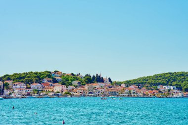 Yamaçta açık mavi sular boyunca yanaşmış tekneleri olan renkli kıyı evleri olan deniz kenarı kasabası. Adriyatik Denizi 'nde yaz tatili için konutlar. Rogoznica, Hırvatistan - 14 Temmuz 2024