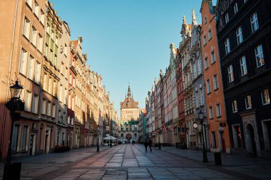 Avrupa 'nın tarihi kaldırım taşı sokağının güzel manzarası açık mavi gökyüzünün altındaki saat kulesine uzanan renkli binalarla dolu. Polonya, Gdansk 'ın mimarisi. Gdansk, Polonya - 10 Nisan 2023