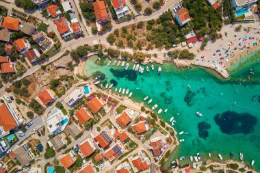 Kırmızı çatılı evleri, turkuaz suları ve kıyı boyunca tekneleri olan kıyı köyünün havadan görünüşü. Hırvatistan 'ın Adriyatik Denizi kıyısındaki Rogoznica kentinin panoraması. Yaz tatili kavramı