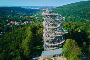 Yeşil orman ve dağların üzerindeki sarmal merdivenli gözlem kulesinin havadan görüntüsü. Polonya, Sweradow Zdroj 'daki Sky Walk gözlem kulesi. Açık hava aktiviteleri ve yürüyüş konsepti