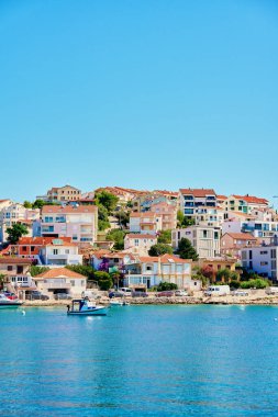 Yamaçta açık mavi sular boyunca yanaşmış tekneleri olan renkli kıyı evleri olan deniz kenarı kasabası. Hırvatistan 'ın Rogoznica kentindeki Adriyatik Denizi' nde yaz tatili için konut