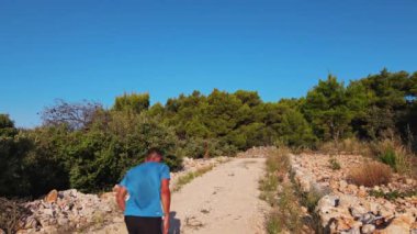 Yeşillik ve açık mavi gökyüzünün altındaki ağaçlarla çevrili kayalık yolda koşan bir adam. Sıcak yaz gününde ülkeyi boydan boya koşan erkek sporcu. Dayanıklılık eğitimi