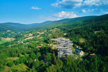 Yeşil orman ve dağların üzerindeki sarmal merdivenli gözlem kulesinin havadan görüntüsü. Polonya, Sweradow Zdroj 'daki Sky Walk gözlem kulesi. Açık hava aktiviteleri ve yürüyüş konsepti
