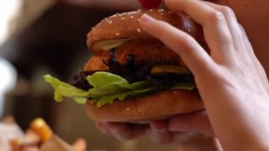 Restoranda salatalı, turşulu ve domatesli tavuk burger yiyen çocuk. Çocuk hamburgeri ısırırken yakın çekim. Aç çocuk sağlıksız yiyecekler yiyor.