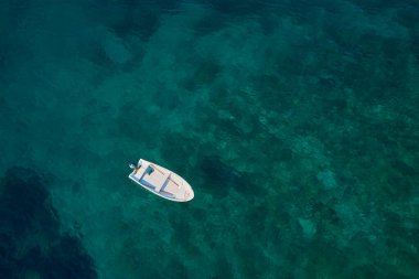 Güneşli yaz gününde şeffaf turkuaz su yüzeyindeki küçük balıkçı teknesinin havadan görünüşü. Denizde bir gemi, üst manzara. Yaz tatili ve turizm konsepti