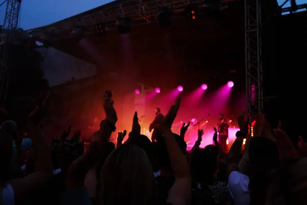 stock image Silhouettes of crowd at concert in front of stage with bright spotlights. People enjoy live music at the bands performance. Concert hall with musicians on stage and fans during music festival