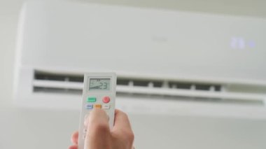 Klima sıcaklığını uzaktan kumandayla ayarlıyorum. Uzaktan kumandalı ve apartmandaki iklim sisteminde rahat sıcaklık ayarlı.