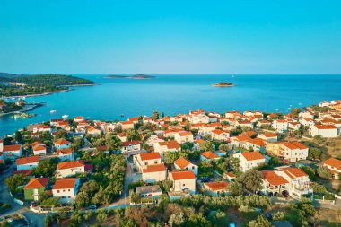 Turkuvaz suyu ve kırmızı çatılı evleri olan kıyı şehrinin deniz manzarası. Hırvatistan 'ın Adriyatik Denizi kıyısındaki Rogoznica kentinin panoraması. Yaz tatili ve seyahat konsepti