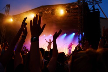 Silhouettes of crowd at concert in front of stage with bright spotlights. People enjoy live music at the band's performance. Concert hall with musicians on stage and fans during music festival clipart