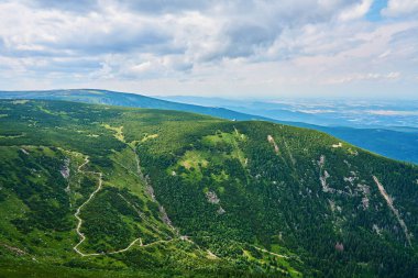 Yeşil dağ vadisinin güzel panoramik manzarası. Yuvarlanan tepeler ve bulutlu gökyüzünün altında sık ormanlar. Seyahat turizmi ve yürüyüş konsepti