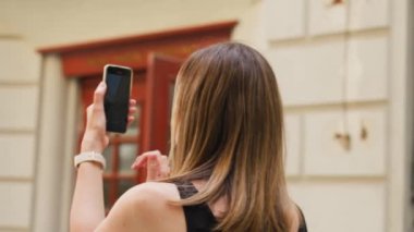 Renkli tarihi binalarla çevrili Avrupa şehir meydanında fotoğraf çeken bir kadın. Dişi turist akıllı telefonuyla seyahat ederken anılarını yakalıyor