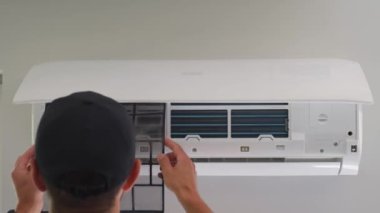 Klima ünitesinin bakımı. Teknisyen, beyaz duvara monte edilmiş klima sistemini kontrol ediyor. Ön kapağı açık olan iklim sistemi iç bileşenleri açığa çıkarıyor. Apartmandaki havalandırma tamir ediliyor.