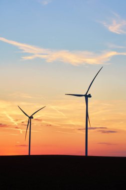 Gün batımında kırsal alanda siluetli rüzgar türbinleri. Rüzgar santrali temiz enerji üretiyor. Yenilenebilir ve sürdürülebilir enerji kavramı