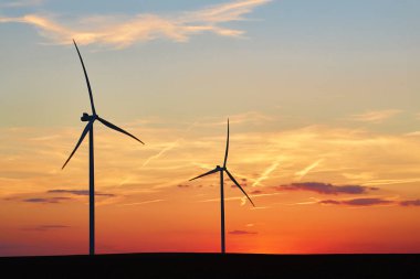 Gün batımında kırsal alanda siluetli rüzgar türbinleri. Rüzgar santrali temiz enerji üretiyor. Yenilenebilir ve sürdürülebilir enerji kavramı