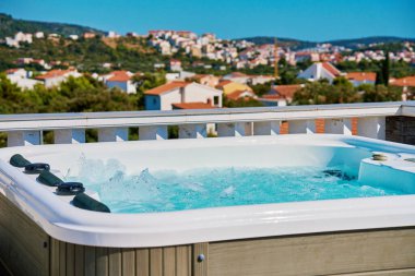 Outdoor hot tub on sunny rooftop deck with bubbling water and comfortable seating with beautiful view on touristic cityscape. Place for relaxation and leisure during summer vacations clipart