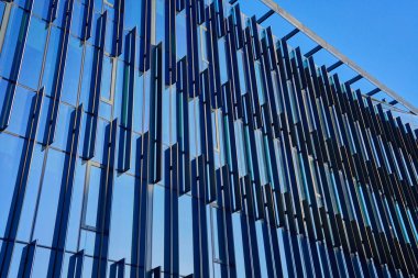 Gökyüzünü yansıtan geometrik desenli modern cam bina cephesine yakın çekim. Çağdaş mimari tasarım.