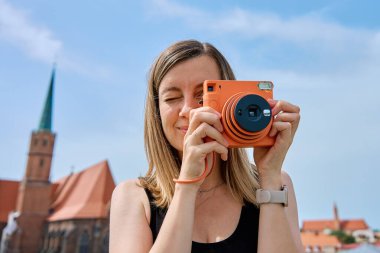 Avrupa şehrinde renkli tarihi binalarla çevrili bir kadın fotoğraf çekiyor. Kadın turist, seyahat sırasında eski moda kamera ile anıları yakalıyor.