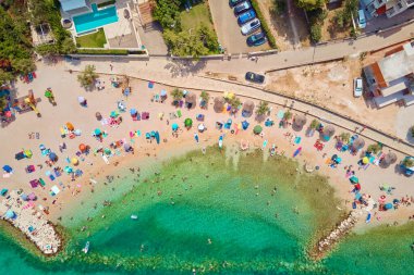 Renkli şemsiyeleri ve rahatlatıcı insanları olan deniz plajı, hava manzaralı. Yüksek mevsimde kalabalık kumlu plajlar. Hırvatistan 'da yaz tatilinde turistler