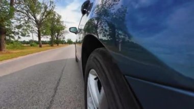 Caddedeki asfalt yolda araba sürerken yakın plan görüntüsü. Aracın tekerlek dönme hareketi