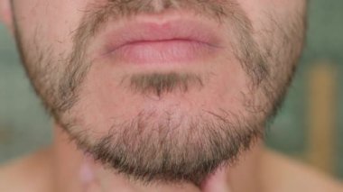 Banyoda traşsız yüzlere dokunan bir adamın aynadaki sakal uzamasını incelerken. Cilt bakımı ve kişisel bakım konsepti
