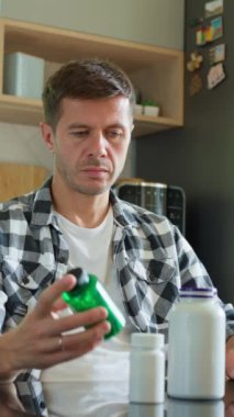 Adam mutfakta masada oturmuş çeşitli ilaç kapsülleri şişelerine bakıyor. İnsan ilaç ya da vitamin alıyor. İlave, ilaç veya sağlık hizmetleri kavramı