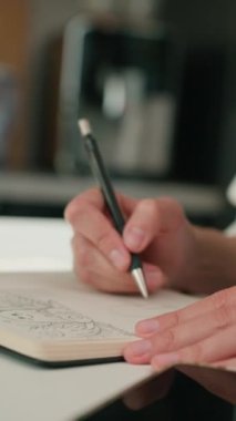Defterde çizim yapan kişi uzaktan bilgisayarla masa başında çalışıyor. Ev ofisinde serbest bir iş. Grafik tasarımcısı çizimi