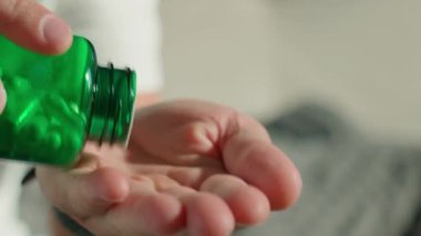 Yeşil şişeden beyaz kapsülleri eline döken adama yakın çekim. İnsan ilaç ya da vitamin alıyor. İlave, ilaç veya sağlık hizmetleri kavramı