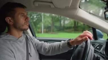 Yağmurlu bir günde araba süren adam yola odaklanıyor. Sürücü erkek, trafiğe bakıyor ve direksiyonu çeviriyor. Güvenli sürüş