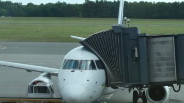 Yolcu uçağı, bağlı jet köprüsü ve yer destek aracı ile havaalanı kapısına yanaştı. Beyaz uçağa binen yolcular