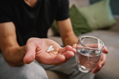 Adam bir elinde iki hap, diğer elinde bir bardak su tutuyor. İnsan beslenme takviyeleri ve vitaminler alır. Sağlığı korumak için günlük tıbbi prosedür