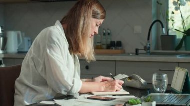 Mutfakta dizüstü bilgisayarı ve fatura destesiyle oturan stresli kadının portresi. Kadın planlama ev bütçesi, finans faturası ve hesaplama giderleri