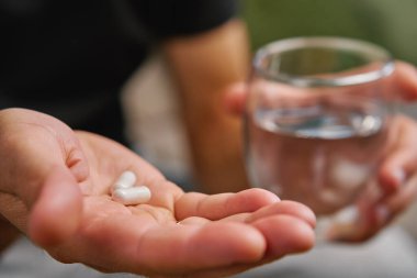 Adam bir elinde iki hap, diğer elinde bir bardak su tutuyor. İnsan beslenme takviyeleri ve vitaminler alır. Sağlığı korumak için günlük tıbbi prosedür