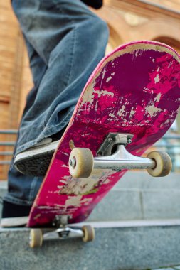 Pembe kaykayın üstünde dengede duran kaykaycının alçak açılı görüntüsü. Güvertenin altını ve şehir caddesindeki merdivenlerde kaykay tekerleklerini kapatın.