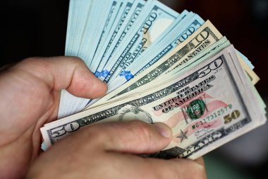 El ele tutuşup banknotları sayıyoruz. Amerikan dolarlarını elinde tutan adam. Para yönetimi, zenginlik veya mali işlemler kavramı