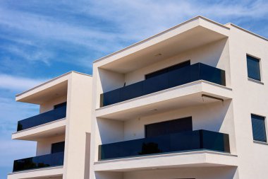 Parlak mavi gökyüzüne karşı camdan balkonları olan modern apartmanın yakın çekimi. Minimalist tarzda konut binasının soyut görüntüsü. Çağdaş mimarinin ayrıntıları