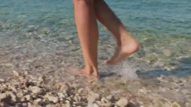 Deniz kıyısında çıplak ayakla yürüyen kadın turist yaz tatilinin tadını çıkarıyor, suda ayaklarını dinlendiriyor. Çakıl taşlı sahil boyunca yürüyen bir kadın.