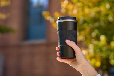 Bulanık sonbahar arka planında yeniden kullanılabilir kahve fincanı tutan kadın. Sürdürülebilir ve çevre dostu yaşam kavramı