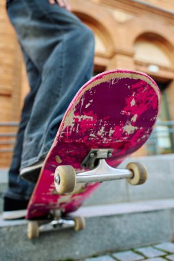 Pembe kaykayın üstünde dengede duran kaykaycının alçak açılı görüntüsü. Güvertenin altını ve şehir caddesindeki merdivenlerde kaykay tekerleklerini kapatın.