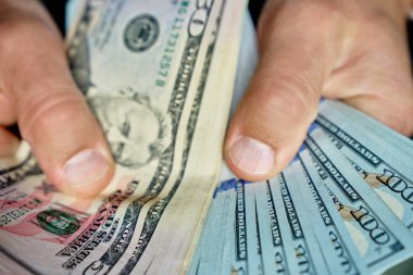 El ele tutuşup banknotları sayıyoruz. Amerikan dolarlarını elinde tutan adam. Para yönetimi, zenginlik veya mali işlemler kavramı