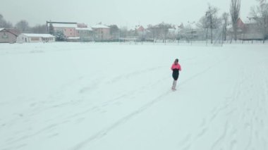 Stadyumda karla kaplı pistte koşan bir kadın. Karlı yolda koşan bir bayan sporcu. Kış sporları eğitimi kavramı