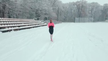 Stadyumda karla kaplı pistte koşan bir kadın. Karlı yolda koşan bir bayan sporcu. Kış sporları eğitimi kavramı
