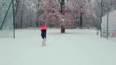 Stadyumda karla kaplı pistte koşan bir kadın. Karlı yolda koşan bir bayan sporcu. Kış sporları eğitimi kavramı