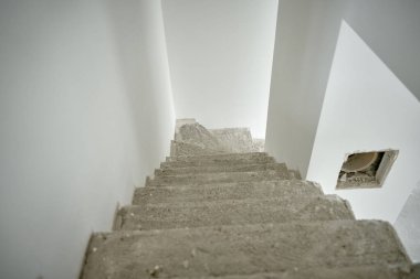 Tamamlanmamış beton merdivenleri ve tadilattan geçen beyaz duvarları olan boş bir daire. İnşaat halindeki binanın içi.
