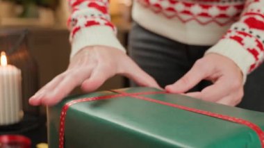 Noel hediyelerini kırmızı ve yeşil kağıda saran kadın elleri. Şenlikli kazaklı kadın kış tatili için hediyeler hazırlıyor. Noel ve Yeni Yıl Aile Gelenekleri