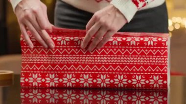 Noel hediyelerini kırmızı ve yeşil kağıda saran kadın elleri. Şenlikli kazaklı kadın kış tatili için hediyeler hazırlıyor. Noel ve Yeni Yıl Aile Gelenekleri